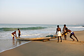 Fischer schieben ihr Boot vom Strand ins Wasser; Kovalam, Kerala, Indien