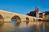 Old 12th Century Stone Bridge and the Gothic St Peter's Cathedral (Regensburg Cathedral) at the Danube River in the Old Town of Regensburg with a blue sky in Autumn; Regensburg, Upper Palatinate, Bavaria, Germany