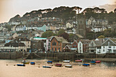Small boats are anchored in front of the small coastal town of Fowey, Cornwall, England.