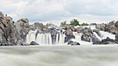 A kayaker stands next to Great Falls waterfall and asseses the river before going over it.
