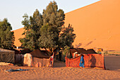 A Moroccan man walks among a tented camp located in the Sahara desert.; Erg Chebbi , Sahara Desert , Morocco
