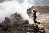 Eine Frau spaziert zwischen den dampfenden Schlammtöpfen im geothermischen Gebiet in der Nähe des Myvatn-Sees; Island