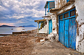 Verfallene Steingebäude mit bemalten, blauen Holztüren neben dem Ufer mit Bergen am Horizont in der Dämmerung