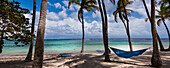 Türkisfarbenes Wasser der Karibik mit weißen, bauschigen Wolken am blauen Himmel und einer blauen Hängematte zwischen den Kokosnusspalmen am Caravelle Beach, Sainte-Anne auf Grande-Terre; Guadeloupe, Französisch-Westindien