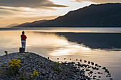 At sunrise, a man looks at calm lake waters of Loch Ness in Scotland; Fort Augustus, Scotland