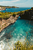 Green covered sea arch, rock formation with the turquoise water and ocean surf along the rocky coastline in the Nusa Islands; Nusa Penida, Province of Bali, Indonesia