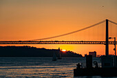 Silhouette der Brücke 25 de Abril über den Tejo, die Lissabon und Almada bei Sonnenuntergang verbindet; Lissabon, Estremadura, Portugal