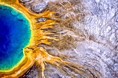 Grand Prismatic Spring ist eines der größten und schönsten Beispiele für eine häufige hydrothermale Erscheinung im Yellowstone-Nationalpark und eine der größten heißen Quellen in den Vereinigten Staaten. Die prismatischen, farbenfrohen Merkmale stammen aus mehreren Quellen; das tiefe Blau in der Mitte ist das klare, überhitzte Wasser, das von der unterirdischen Wärmequelle nach oben zirkuliert und ein Paar Konvektionsströme wie ein Augenpaar zeigt. Wenn das Wasser an den Rändern des Beckens und auf den Sinterterrassen abkühlt, erzeugen Bakterien und Algen den Regenbogen der Farben. Diese heiße