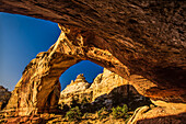 Underneath the Hickman Natural Bridge looking through the arch at the sandstone cliffs in the Capitol Reef National Park; Utah, United States of America
