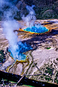 Der Excelsior Geysir Krater liegt etwa 100 Meter nördlich der Grand Prismatic Spring und ist eine der Hauptattraktionen des Yellowstone Nationalparks. Der Excelsior Geysir brach zuletzt in den 1880er Jahren aus, wobei er Wasser bis zu 300 Fuß hoch schleuderte und genug Wasser ausstieß, um den Pegel des nahe gelegenen Firehole River um bis zu einem Fuß anzuheben. Der Excelsior Geysir-Krater produziert immer noch eine beeindruckende Menge an heißem Wasser, etwa 3000 Gallonen pro Minute; Yellowstone National Park, Wyoming, Vereinigte Staaten von Amerika