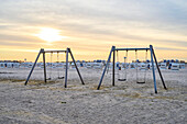 Swing sets on a sandy beach with Strandkorb beach chairs in the background at sunrise along the North Sea at a seaside resort in North Friesland; Sankt Peter-Ording, Schleswig-Holstein, Germany