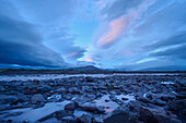 Gletscherfluss, der durch die Basaltlandschaft fließt, mit einem dramatischen Wolkenhimmel bei Sonnenuntergang entlang des Kaldidalur-Tals; Husafell, Nordurland Vestra, Island