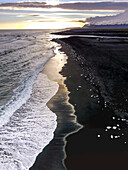 An aerial view of foamy surf and the ice from the Jokulsarlon Glacier Lagoon washing up on a black sand beach; Jokulsarlon, Vatnajökull National Park, Iceland