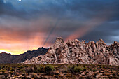Crepuscular rays at sunset behind rock formations in the Mojave Desert; Kelso, California, United States of America