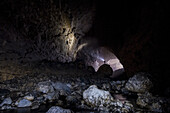 A man stands on a boulder and shines his headlamp onto the walls of a cave in China.