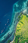 Blick von oben auf Boote, die vor einer Insel im Komodo-Nationalpark vertäut sind, mit einem Pier, der in das türkisfarbene Wasser hineinragt; East Nusa Tenggara, Kleine Sunda-Inseln, Indonesien