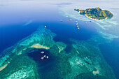 Luftaufnahme von Booten, die eine Insel und eine vorgelagerte Lagune im Komodo-Nationalpark umfahren; East Nusa Tenggara, Kleine Sunda-Inseln, Indonesien