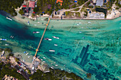 Aerial of boats on the waterway passing under the iconic Yellow Bridge connecting Nusa Lembongan and Nusa Ceningan, also showing the underwater patches of seaweed  farming under the shallow, turquoise water; Klungkung Regency, East Bali, Bali, Indonesia