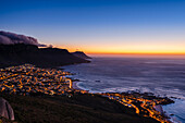 Cloud formation creating table cloth effect over the Twelve Apostles mountain range with an overview of Cape Town city skyline and view of Camps Bay along the Atlantic Ocean Coast at sunset; Cape Town, Western Cape Province, South Africa