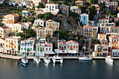 Überblick über pastellfarbene Gebäude und Segelboote entlang der Uferpromenade am Hafen von Gialos, Insel Symi (Simi); Dodekanes-Inselgruppe, Griechenland