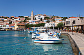 Traditionelle Gebäude und Fischerboote entlang der Uferpromenade im Hafen von Emborio, dem Hauptort der Insel Chalki (Halki); Dodekanes-Inselgruppe, Griechenland