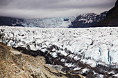 Distant hikers dwarfed by a massive Icelandic glacier.; Svinafellsjokull Glacier, Skaftafell National Park, Iceland.