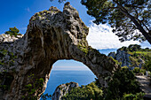 View through the Arco Naturale, a Palaeolithic era limestone arch, remains of a collapsed grotto, 18m high, span of 12m, on the east coast of the Island of Capri; Naples, Capri, Italy