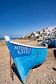 Traditional, bright blue fishing boats line the beach at Taghazout Village with the whitewashed buildings on the hillside in the background; Taghazout Bay, Agadir, Morocco