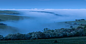 The last rays of the sun glance the top of a bank of sea fog that has poured in from the English Channel and settled in the hollows and valleys of the South Downs National Park; Brighton, East Sussex, England, United Kingdom