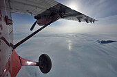 Blick nach vorne auf die Vorderseite des Twin Otter Flugzeugs mit dem Rad und der Tragfläche im Bild. Nichts als Eis und Wolken ziehen vorbei; Nordostgrönland , Grönland