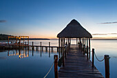 Silhouette of Tiki hut gazebo on dock at Rancho Encantado Eco-Resort & Spa in Bacalar at sunrise; Quintana Roo, Mexico