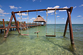 Swing set and Tiki hut gazebo on dock with turquoise water at Rancho Encantado Eco-Resort & Spa in Bacalar; Quintana Roo, Mexico