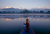 Eine Frau in einem Ruderboot blickt auf die Annapurna Range in der Morgendämmerung; Annapurna Range, Himalaya Gebirge, Nepal.