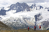 Hikers on a ridge line with snow covered peaks in the background; Adamants Mountain Range, British Columbia, Canada