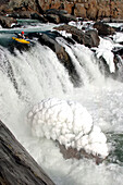 Ein winterlicher Wildwasserkajakfahrer am Rande eines großen Wasserfalls und Eis; Great Falls, Potomac River, Maryland.