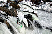 Wildwasserkajakfahrer durchfährt einen fast gefrorenen Wasserfall im Winter; Great Falls, Potomac River, Maryland.