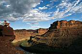 Wanderer sitzt am Rande einer Klippe und überblickt den Colorado River; Cataract Canyon, Utah.