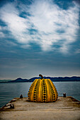 The Naoshima Pumpkin is a sculpture in the form of a giant black and yellow polka-dotted pumpkin by the celebrated artist Yayoi Kusama. It has stood at the end of a pier on the “art island” of Naoshima in the Seto inland sea since 1994.  The sculpture was damaged in a storm in April 2021 and was repaired and reinstalled in  October, 2022; Naoshima Island, Seto Inland Sea, Japan