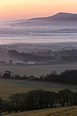 Der Sonnenaufgang wirft pastellfarbene Schatten über eine morgendliche Nebelinversion, die über der englischen Landschaft liegt; Lewes, East Sussex, England, Vereinigtes Königreich