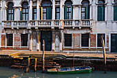 Holzboot an einem Poller vor einem alten Steingebäude entlang des Kanals in Venetien; Venedig, Italien