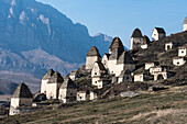 Abandoned village with traditional conical roofed shelters on the mountainside in Ingushetia with jagged mountain ridges in the background; Republic of Ingushetia, Russia