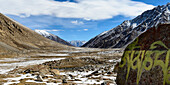 Icy valley with mantra painted on rock and snow capped mountains behind in the foothills of the Himalayas in the Ladakh Region; Jammu and Kashmir, India