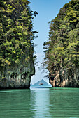 Blick auf eine Yacht, die im grünen, türkisfarbenen Wasser ankert, zwischen riesigen Karstfelsen, die eine ruhige Szene schaffen; Phang Nga Bay, Thailand