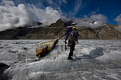 Ein Expeditionsleiter trägt die Ausrüstung auf dem Weg zum Abstieg in eine Gletschermühle und zur Erkundung des Aletschgletschers.