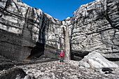 Woman watching a waterfall plunging from a glacier wall while exploring the landscape around a glacier in the South of Iceland; Vik, South Iceland, Iceland