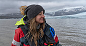 Close-up view of a woman with blond hair, wearing a woolen hat, enjoying a boat tour on Fjallsárlón Glacier Lagoon; South Iceland, Iceland