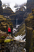 Frau steht und überblickt die Mulagljufur-Schlucht, ein Wanderparadies, mit erstaunlichem Blick auf einen Wasserfall und die moosbewachsenen Klippen; Vik, Südisland, Island