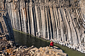 Woman standing on the edge of a rocky cliff looking at the basalt columns of Stuðlagil Canyon in Northeastern Iceland, creating an amazing and surreal landscape; Stuðlagil Canyon, North Iceland, Iceland