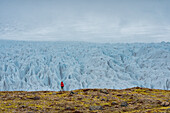 Woman walking on the tundra in front of an impressive glacier with its jagged blue ice and foggy atmosphere along the South Coast of Iceland; South Iceland, Iceland