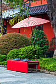 Roter Regenschirm über einer Bank außerhalb eines Tempels; Tokio, Japan